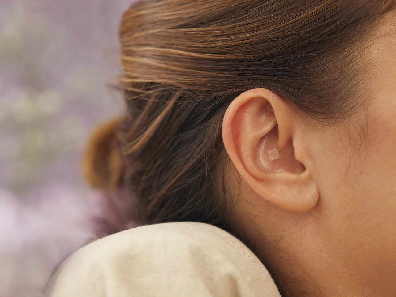 Close-up of an outer ear with a small adhesive ear seed in a restful setting.
